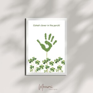 Op de afbeelding: Een groene handafdruk op een witte achtergrond met de tekst "Cutest clover in the porch!" erboven. Groene klaverblaadjes bevinden zich onderaan de afbeelding.