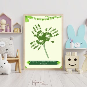 Op de afbeelding: Een groene klaver gemaakt van handafdrukken met een groene stengel en bladeren. De klaver bevindt zich op een lichtgele achtergrond met een groene banner waarop staat "Ik ben blij om van je te houden - Mijn grootste schat!"