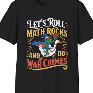 May include: Black t-shirt with a whimsical graphic. The design features a frog in a wizard hat riding a goose, holding a basketball. Text reads "Let's Roll Math Rocks and Do War Crimes" in yellow, red, and white.