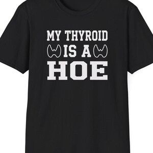 May include: Black t-shirt with white text that reads "MY THYROID IS A HOE". The text is in a bold, sans-serif font. The shirt has short sleeves and a crew neck.
