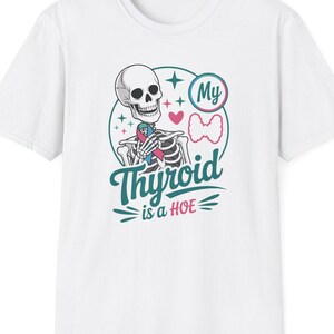 May include: White t-shirt featuring a skeleton graphic holding a heart. The design includes the text "My Thyroid is a HOE" in teal and pink, with a bow and star accents. The shirt is a casual wear item.