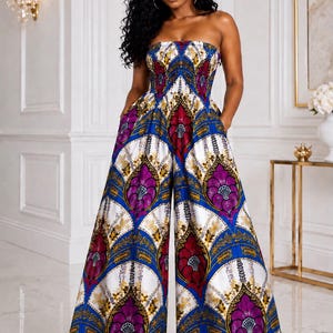 May include: A strapless jumpsuit featuring a vibrant, repeating geometric pattern in shades of royal blue, magenta, white, and gold. The garment has a fitted bodice, a cinched waist, and wide-leg trousers with side pockets, creating a fluid silhouette.