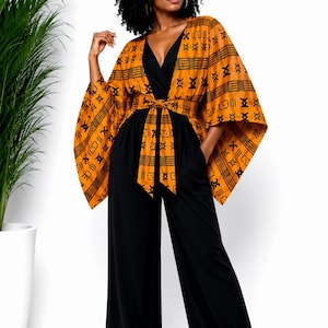 May include: A woman wearing a black jumpsuit with a V-neck and wide legs. The outfit is accented with a patterned, orange and black kimono-style top and matching belt. The kimono features geometric designs.