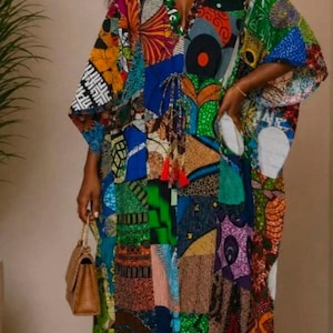 May include: A floor-length kaftan dress featuring a vibrant patchwork design with various geometric and organic patterns in shades of green, blue, orange, and yellow. The garment has a V-neckline, wide sleeves, and a drawstring waist with red tassels.