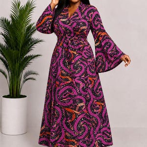 May include: A floor-length wrap dress featuring a vibrant purple, orange, and black snake-inspired pattern. The garment includes long, flared bell sleeves, a V-neckline, and a matching fabric tie belt at the waist, creating a flowing silhouette.