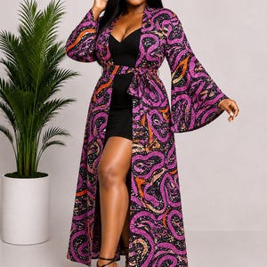 May include: A floor-length open-front duster robe featuring a vibrant purple, black, and orange abstract snake-like pattern, long flared sleeves, and a matching fabric tie belt, worn over a simple black mini dress with thin shoulder straps.