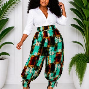 May include: A woman wearing a white button-down shirt and high-waisted, patterned pants. The pants feature a colorful geometric design in teal, brown, and black. The pants have a gathered ankle detail. She is wearing black high heels.