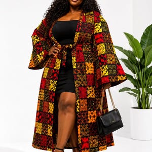 May include: A woman wearing a long, patterned kimono-style robe with a belt. The robe features a patchwork design in red, yellow, and black. She is also wearing a black dress, black heels, and carrying a black purse with a gold chain.