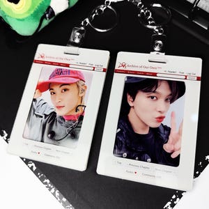 May include: Two white ID badge holders with keychains, each featuring a photo of a person. The badges have the text "Archive of Our Own" and website navigation elements. One person wears a red cap, the other a black hat.