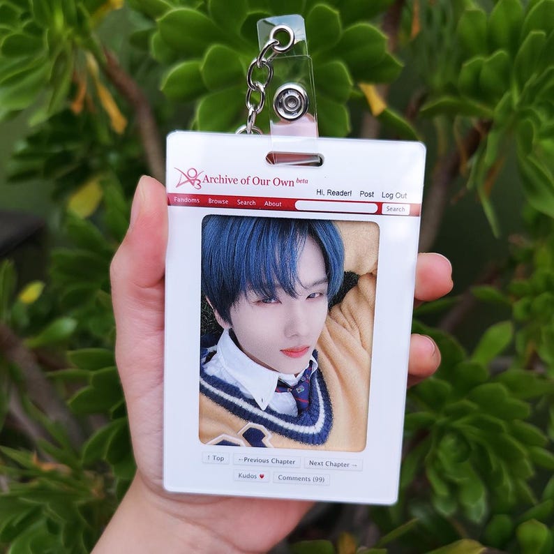May include: A white plastic ID badge with a photo of a person with blue hair. The badge has a clear plastic clip and chain. The text "Archive of Our Own" is printed at the top, with other text below.