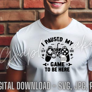 May include: A white t-shirt with a black graphic of a video game controller and the text "I paused my game to be here".