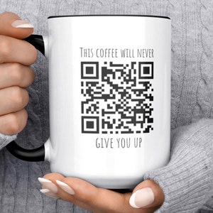 Op de afbeelding: Een witte keramische koffiemok met een zwarte rand en handvat. De mok heeft een zwart-witte QR-code met de tekst "This coffee will never give you up".