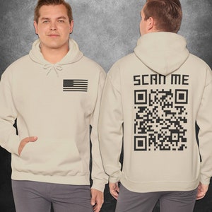 May include: A beige hoodie with a black American flag on the left chest and a black QR code with the text "SCAN ME" on the back.