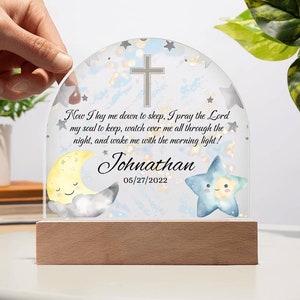 May include: A white nightlight with a blue and white watercolor background. The nightlight features a cross, a crescent moon, and a star. The text "Now I lay me down to sleep, I pray the Lord my soul to keep, watch over me all through the night, and wake me with the morning light!" is printed on the nightlight. The name "Johnathan" and the date "05/27/2022" are also printed on the nightlight.