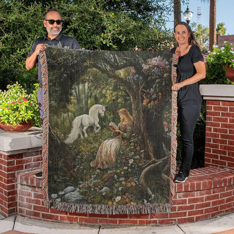 Peut inclure: Une tapisserie murale repr&eacute;sentant une licorne blanche et une femme lisant un livre dans un d&eacute;cor de for&ecirc;t. La tapisserie est de couleur verte, marron et violette avec des d&eacute;tails floraux.