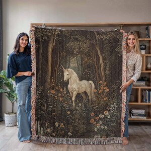 K&ouml;nnte beinhalten: Eine Wanddecke aus Gobelin mit einem wei&szlig;en Einhorn, das in einem dunklen Wald mit gr&uuml;nem und braunem Laub steht. Das Einhorn hat ein goldenes Horn und ist von Blumen umgeben.