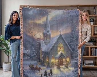 May include: A woven tapestry blanket featuring a winter church scene with a horse-drawn carriage and figures walking in the snow. The blanket has a fringed edge with shades of pink, orange, and beige. The church has a tall steeple and stained-glass windows.