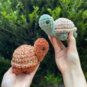May include: Two crocheted turtle toys. One is green and brown, the other is orange and brown.