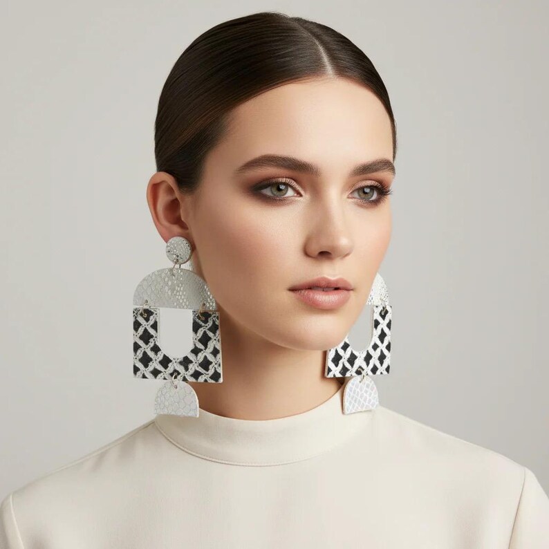 Pode incluir: Uma mulher usando brincos geom&eacute;tricos grandes. Os brincos s&atilde;o prateados e brancos com um design em preto e branco. Eles t&ecirc;m uma superf&iacute;cie texturizada e uma forma &uacute;nica, adicionando um toque ousado ao visual.