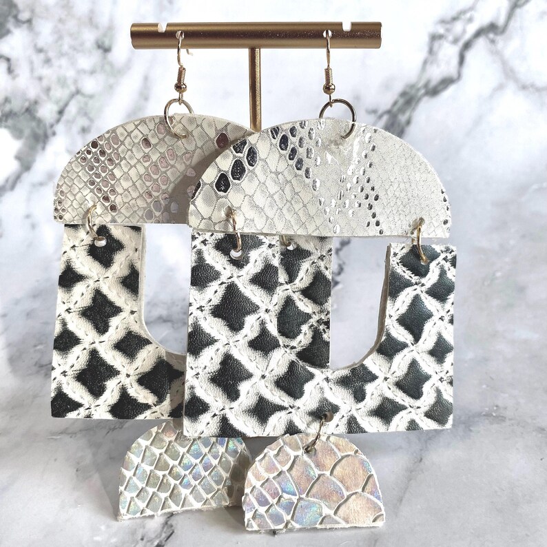 Pode incluir: Tr&ecirc;s pares de brincos pendurados com um design geom&eacute;trico. As se&ccedil;&otilde;es superior e inferior apresentam um padr&atilde;o de pele de cobra em tons de branco e cinza. A se&ccedil;&atilde;o do meio apresenta um padr&atilde;o geom&eacute;trico em preto e branco. Os brincos s&atilde;o suspensos por ganchos dourados.