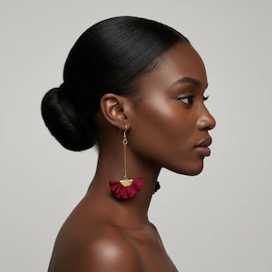 Puede incluir: Elegantes pendientes burdeos con un detalle dorado. Los pendientes presentan un diseño en forma de abanico con un aspecto texturizado y con volantes. Cuelgan de un delicado gancho dorado.