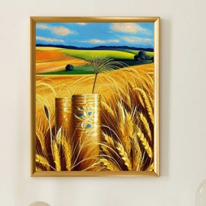 Può includere: Dipinto incorniciato di un campo di grano sotto un cielo blu. Due vasi cilindrici dorati con dettagli blu in primo piano. Una candela d'oro alta e un piccolo orologio su una superficie bianca.