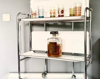 Carrito de servicio plegable blanco de dos niveles, estilo mediados de siglo, fabricado en Alemania. Carrito de bebidas con acabado cromado muy estético y ruedas macizas. Artículos de bar.