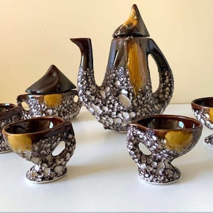 May include: A brown and white ceramic tea set with a teapot, sugar bowl, and four cups. The set has a speckled glaze with brown, white, and yellow accents.
