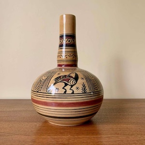 Pode incluir: Um vaso de cerâmica com um design geométrico marrom, preto e vermelho. O vaso tem um corpo redondo e um pescoço estreito.