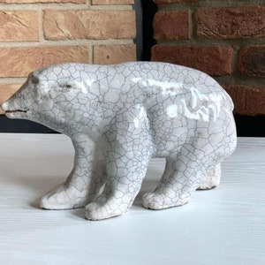 Könnte beinhalten: Eine weiße Keramik-Polarbären-Skulptur mit einer rissigen Glasur. Die Skulptur steht auf einer weißen Oberfläche.