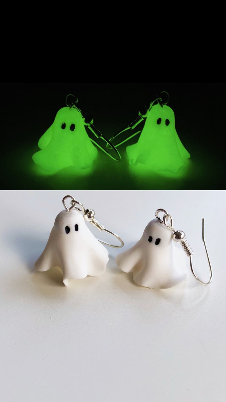 Small handmade ghost sheet jewelry. Top pair of ghost earrings is glowing in the dark, black background. Bottom pair are classic ghost earrings in white. The ghouls have black eyes and appear to float due to organic folds in the sheet.
