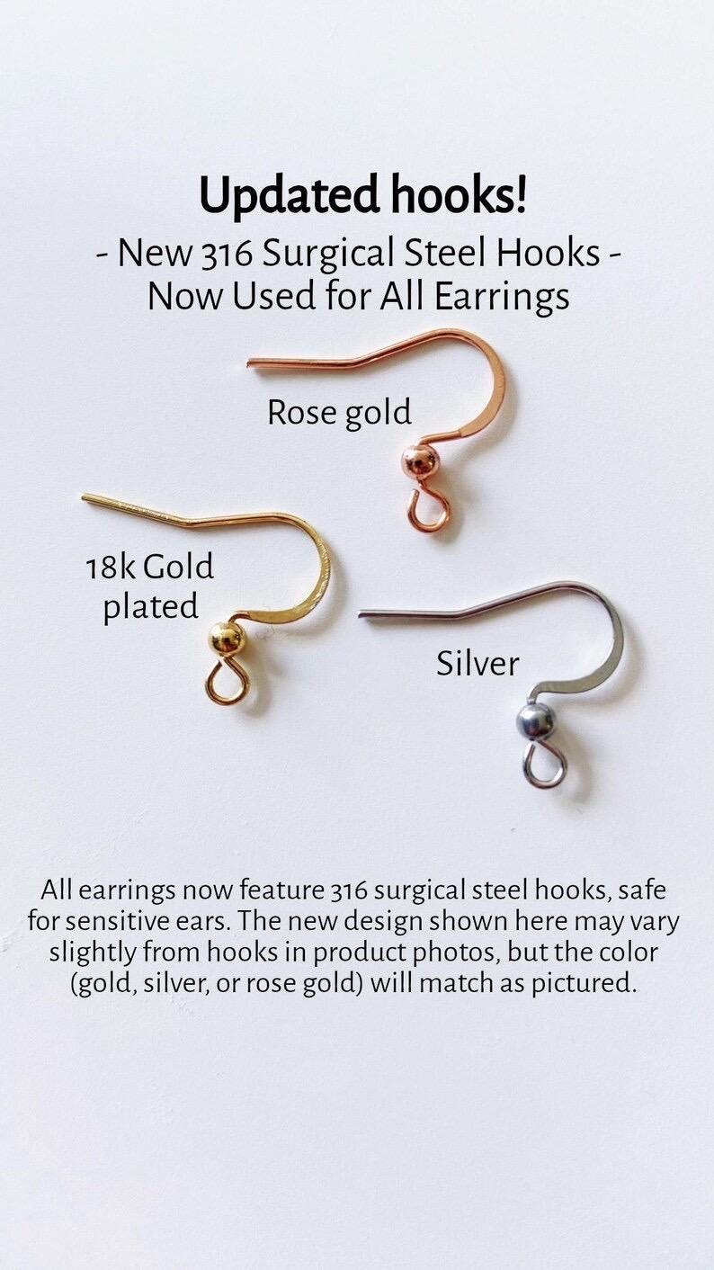 May include: Close-up of three earring hooks in different finishes: rose gold, 18k gold plated, and silver. The text "Updated hooks!" is at the top of the image. The text "New 316 Surgical Steel Hooks - Now Used for All Earrings" is below the hooks. The text "All earrings now feature 316 surgical steel hooks, safe for sensitive ears. The new design shown here may vary slightly from hooks in product photos, but the color (gold, silver, or rose gold) will match as pictured." is at the bottom of the image.