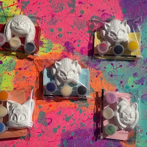 May include: Five individual craft kits, each containing a white moulded character figure, a small paintbrush, and three small paint pots in various colours, all sealed in clear plastic packaging with a coloured card backing behind each figure.