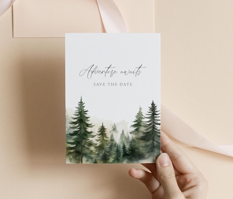 May include: A white card with the text "Adventure awaits" and "Save the date" in elegant script. The bottom of the card features a watercolor painting of a forest with green and gray trees. A hand holds the card against a neutral background.