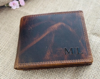 May include: A brown leather wallet with a distressed finish. The wallet has a bi-fold design and features the initials "ML" embossed on the front. The edges are stitched with a contrasting thread, and the wallet appears to be new.