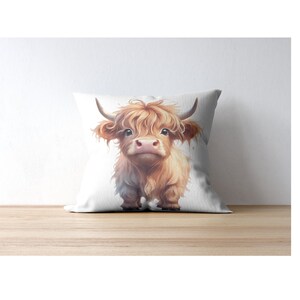 May include: A white pillow with a brown and white Highland cow illustration. The cow is looking directly at the viewer with a friendly expression.