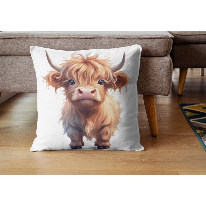 May include: A white pillow with a cute cartoon illustration of a brown and white Highland cow with fluffy hair. The cow is looking directly at the viewer.