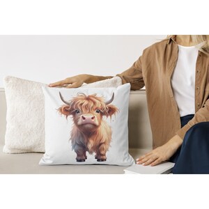 May include: A white throw pillow with a brown and white Highland cow illustration. The cow has a fluffy brown mane and is looking directly at the viewer.