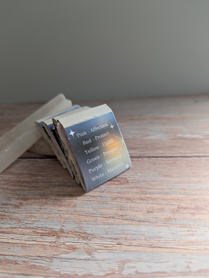 May include: A stack of small, rectangular cards with text and star graphics. The cards are labeled with colors and words like "Affection," "Protect," and "Manifest." The cards are on a wooden surface.