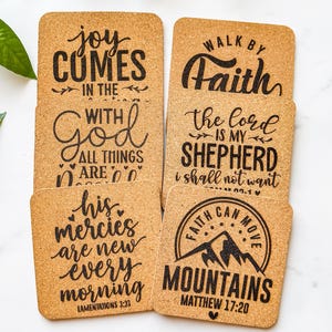 May include: A set of six square cork coasters with black script. The coasters feature inspirational quotes such as "Joy comes in the with God" and "Walk by Faith". One coaster has a mountain graphic with the text "Faith can move mountains".