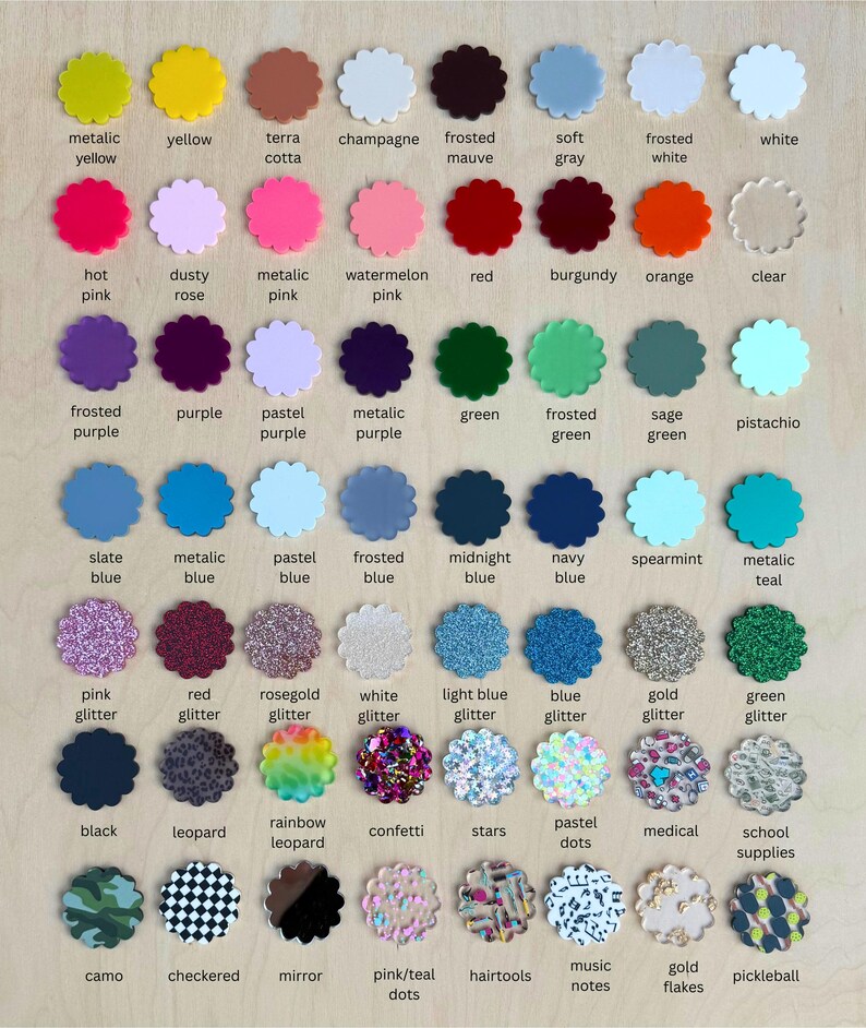 May include: A collection of colorful, scalloped-edge acrylic pieces, each labeled with a color name. Colors range from yellow and pink to blue and green, including glitter and patterned options. The text labels are in a sans-serif font.
