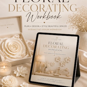 May include: A digital Floral Decorating Workbook by Fleur D'Ivoire displayed on a tablet. The cover features text and images of floral arrangements. Beside the tablet are white fabric flowers, a lit candle, and a box with a large white rose.