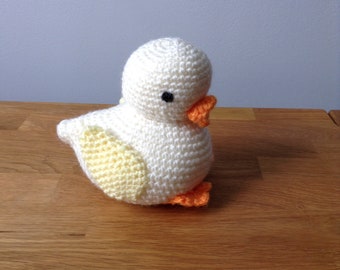 May include: A crocheted white bird with yellow and orange accents. The bird is sitting on a wooden surface.