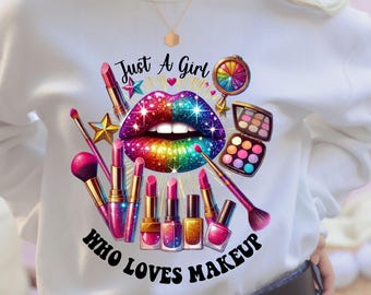 May include: A white sweatshirt featuring a graphic print of rainbow-colored glittery lips, various lipsticks, makeup brushes, a compact mirror, and an eyeshadow palette. The text reads Just A Girl WHO LOVES MAKEUP in black lettering.