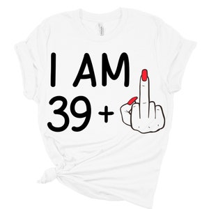 May include: White t-shirt with black text that reads "I AM 39+ " and a black and red cartoon hand giving the middle finger.