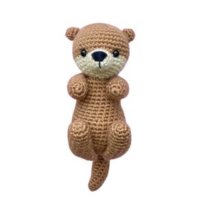 May include: A brown crocheted otter stuffed animal with black eyes and a black nose. The otter is sitting up with its paws in the air and its tail curled behind it.