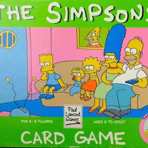 May include: The Simpsons card game box features a bright green border with the title in white. The central illustration shows the Simpson family sitting on a tan couch in a pink room. Text includes Paul Lamond Games, for 3-8 players, and ages 8 to adult.