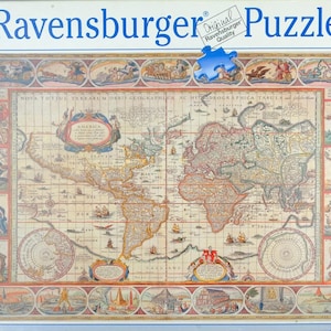 May include: A 2000-piece Ravensburger jigsaw puzzle box featuring an antique-style world map. The box displays the text Ravensburger Puzzle, 2000, and Softclick Technology. The map is surrounded by decorative illustrations of figures and ships.