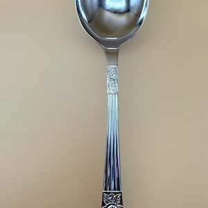 May include: A silver spoon with an oval bowl and a long, decorative handle. The handle features floral designs and vertical lines. The spoon is made of a shiny, reflective metal, possibly stainless steel.