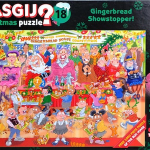 May include: A Wasgij Christmas puzzle box titled Gingerbread Showstopper, featuring a cartoon illustration of a chaotic gingerbread house competition with many characters, a judge in a pink blazer, and a 1000 piece count label.